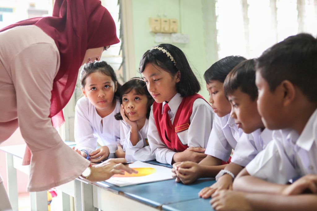 a female teacher teaching a group of students in a classroom